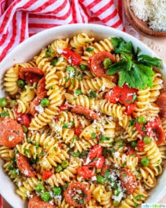 white bowl filled with pasta, tomatoes, herbs, peas, and linguica with red striped napkin..
