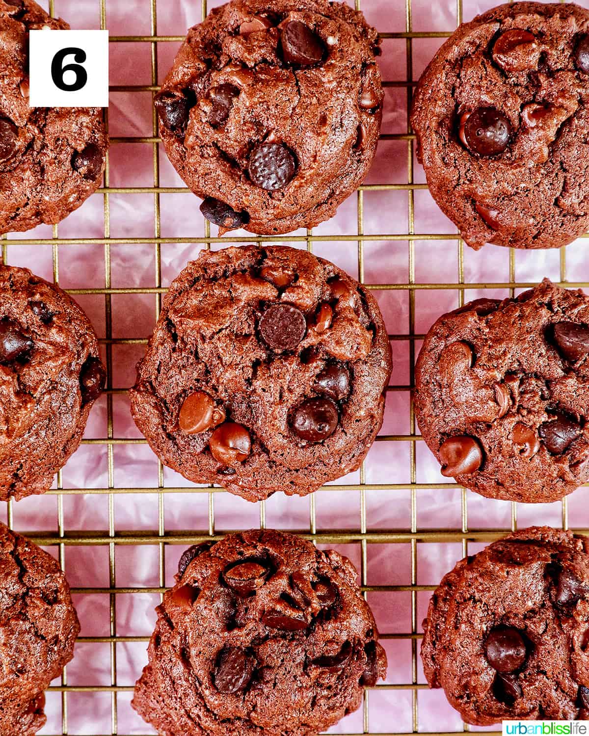three rows of baked chocolate cake mix cookies on a cooling rack on pink table.