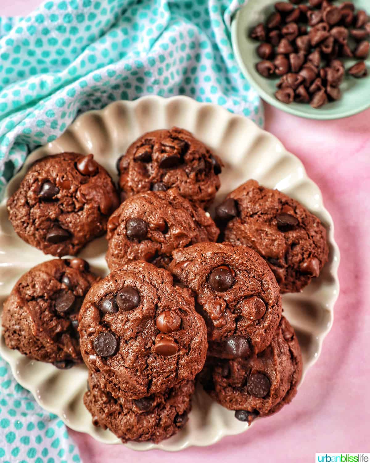 several chocolate cake mix cookies on a scalloped cream colored plate on pink table with blue dotted napkin.