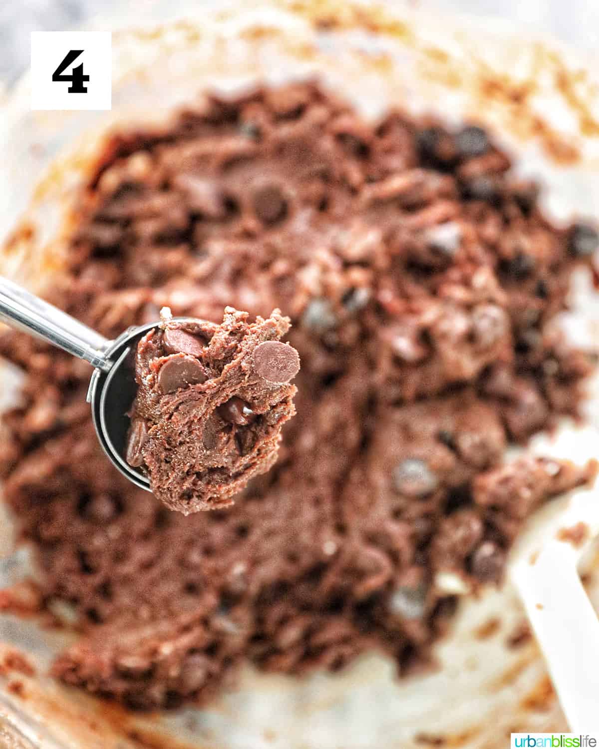 cookie scoop full of chocolate cookie mix with batter in a bowl in the background.