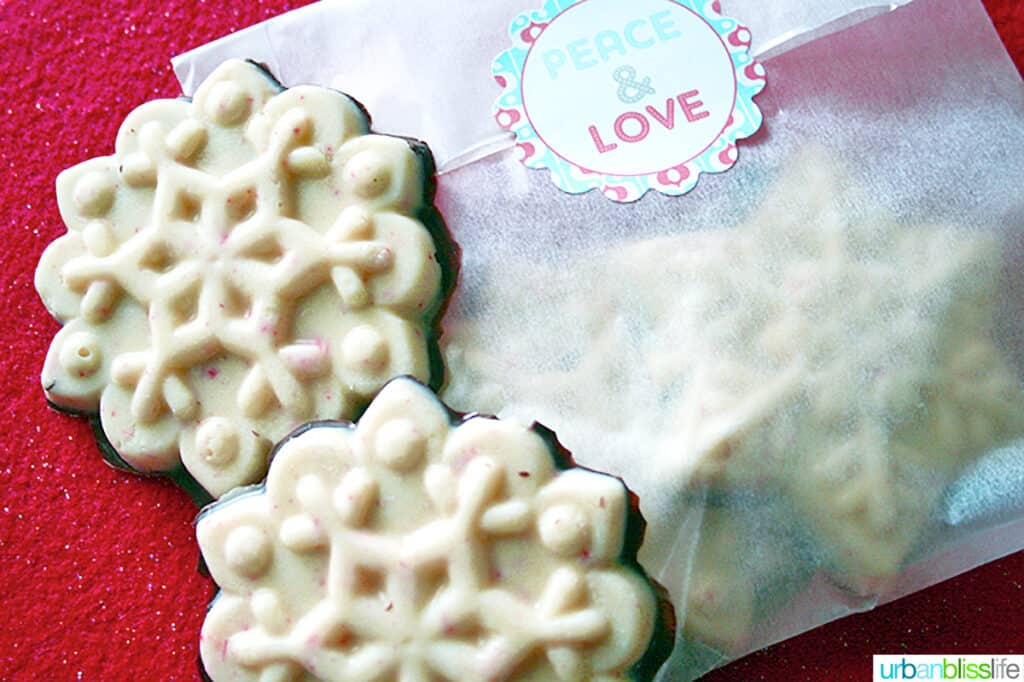 two white chocolate holiday bark in snowflake shapes with wrapped bark next to it.