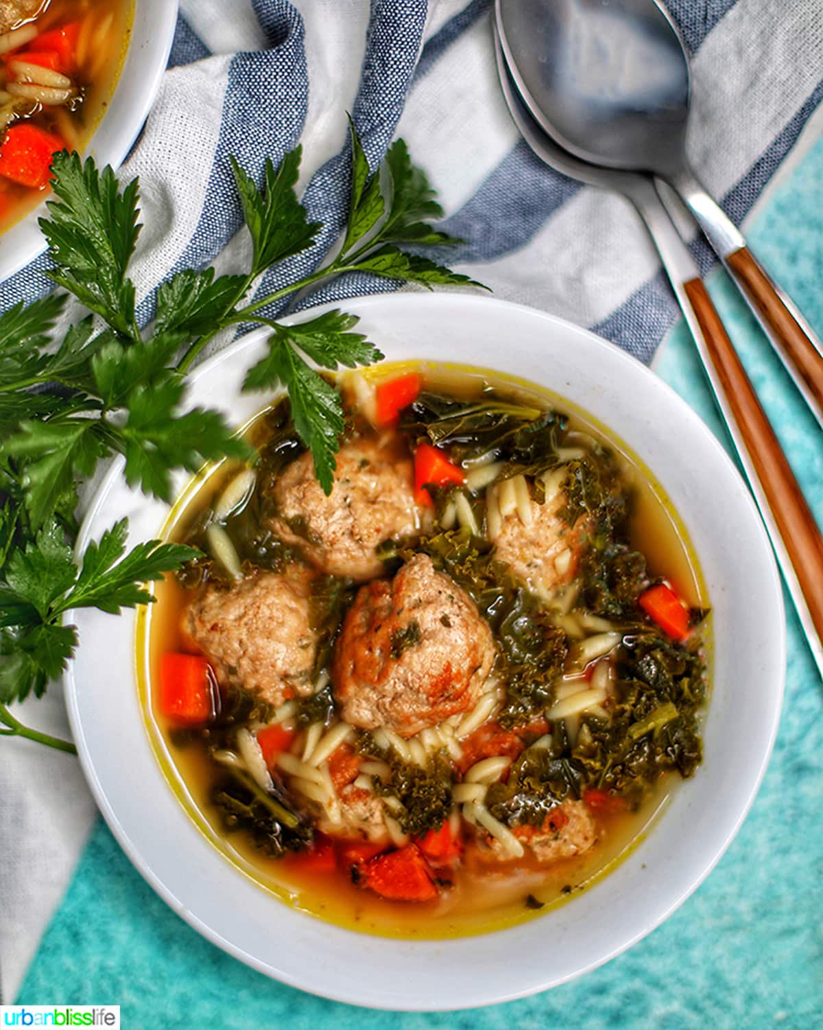 single white bowl of instant pot Italian Wedding Soup with two spoons and parsley garnish.