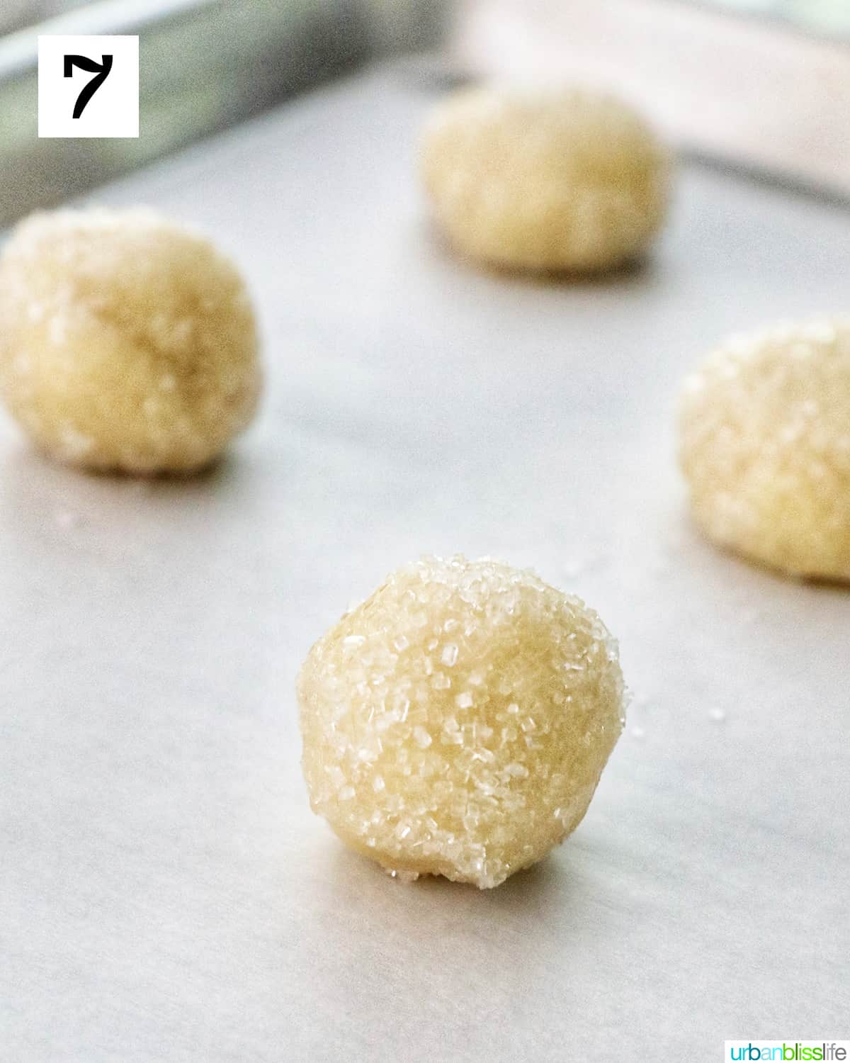 almond sugar cookie dough balls rolled in sanding sugar on a parchment paper lined baking sheet.