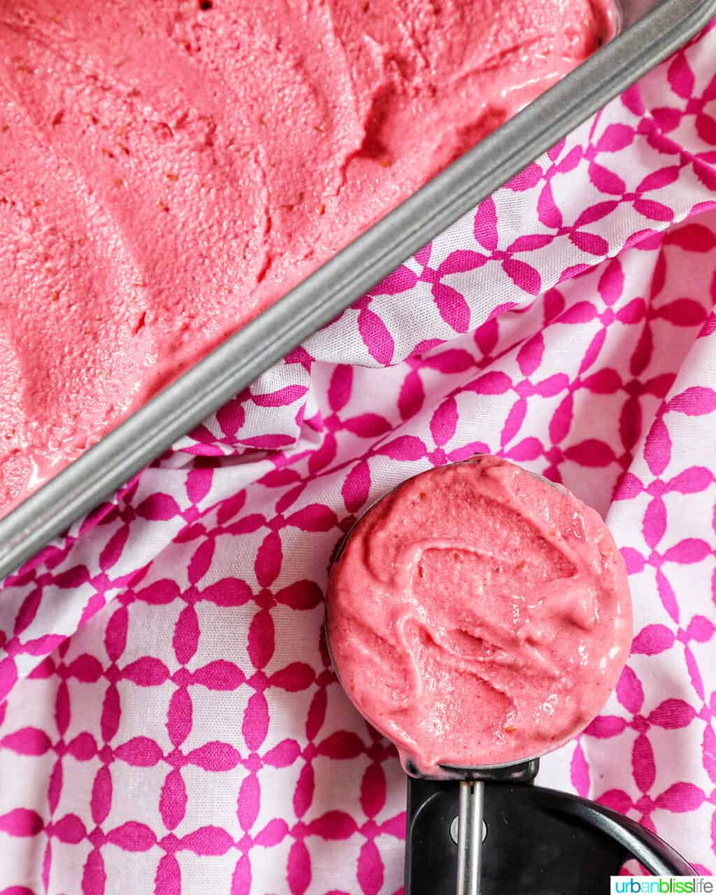 pan full of raspberry sherbet with side of ice cream scoop filled with raspberry sherbet on a pink and white napkin.