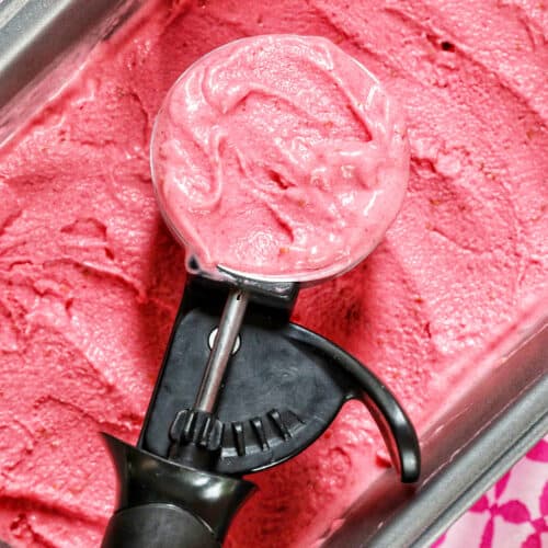 ice cream scoop filled with raspberry sherbet on top of a pan filled with raspberry sherbet.