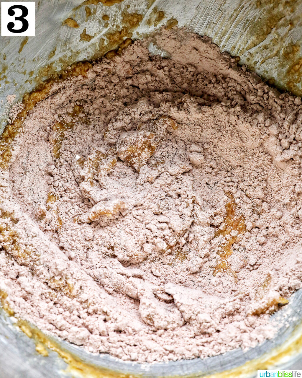 dry and wet ingredients mixing together in a stainless steel bowl of a mixer.