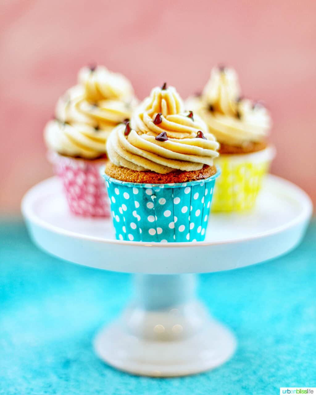 trio of chocolate chip cupcakes with cookie dough frosting in colorful polka dot baking cups on a white pedestal