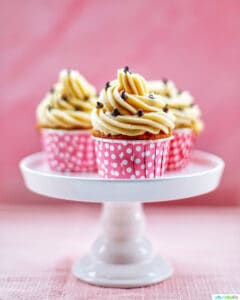 Three Chocolate Chip Cupcakes with Cookie Dough Frosting on a white cake pedestal with pink background