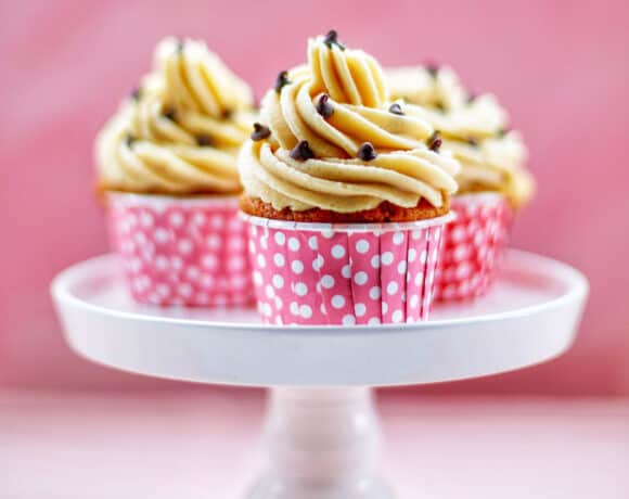 Three Chocolate Chip Cupcakes with Cookie Dough Frosting on a white cake pedestal with pink background