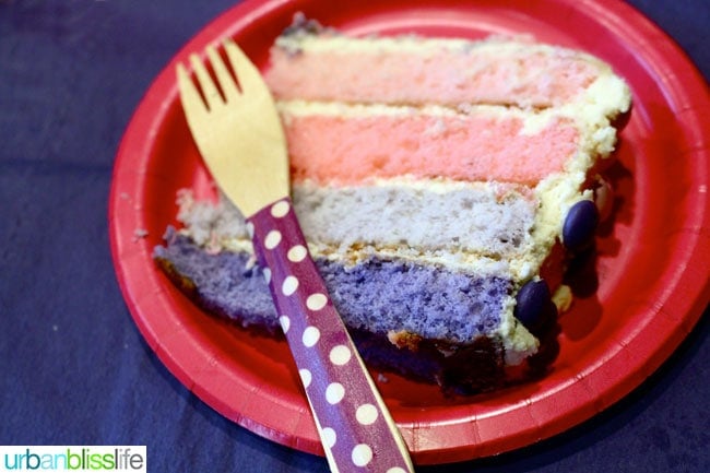 slice of Ombre Cake showing the colored layers on a paper plate with fork.
