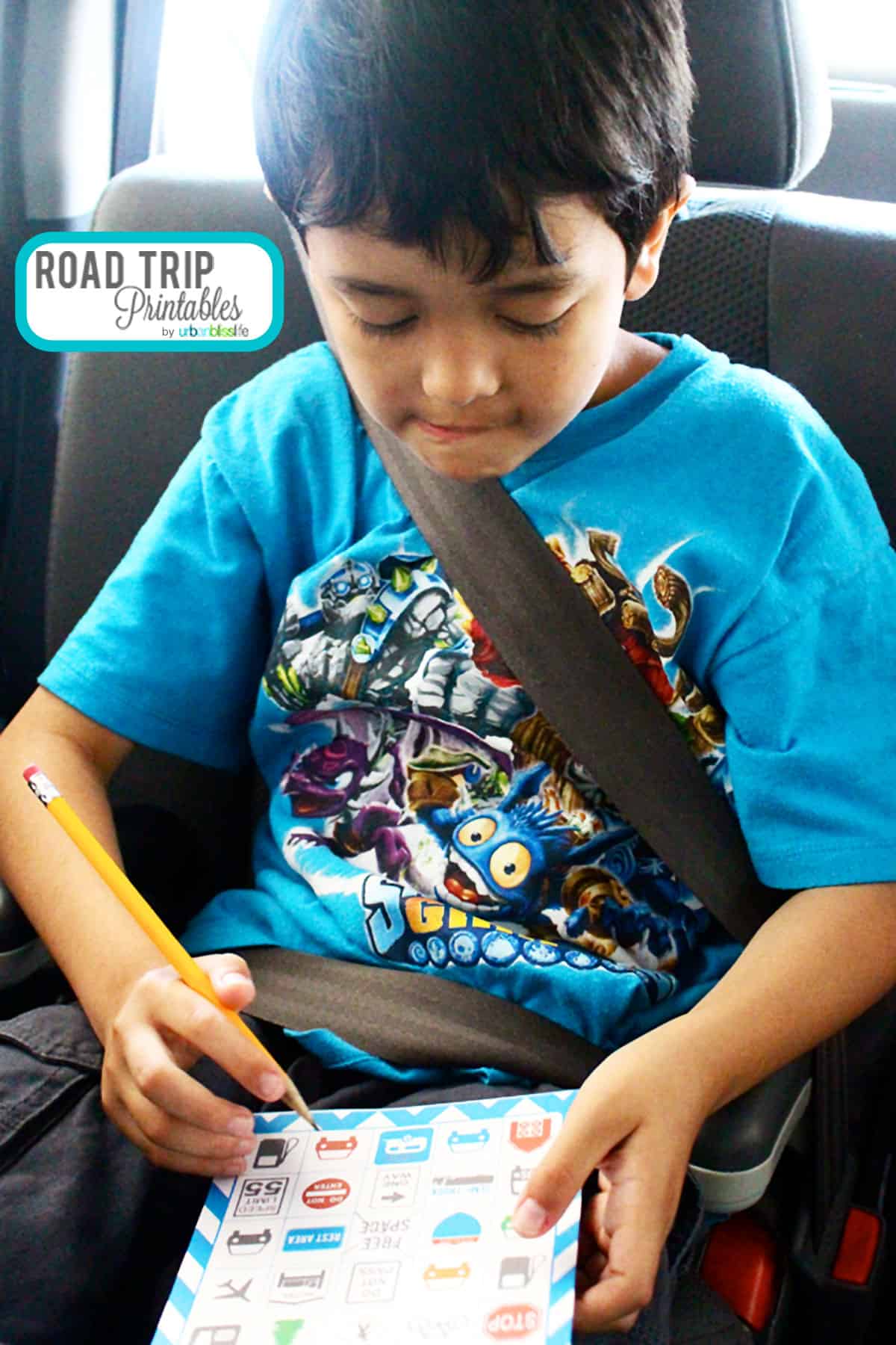 boy writing on a road trip bingo card in a car seat.