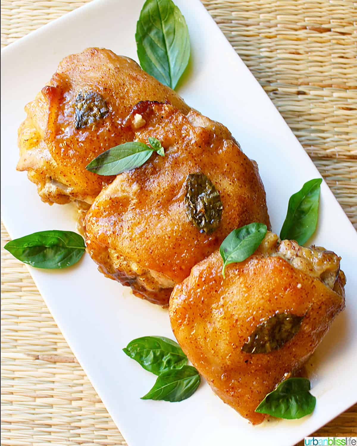Three honey mustard chicken thighs with basil leaves on a white plate.