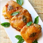 Three honey mustard chicken thighs with basil leaves on a white plate.
