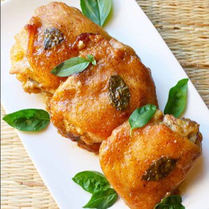 Three honey mustard chicken thighs with basil leaves on a white plate.
