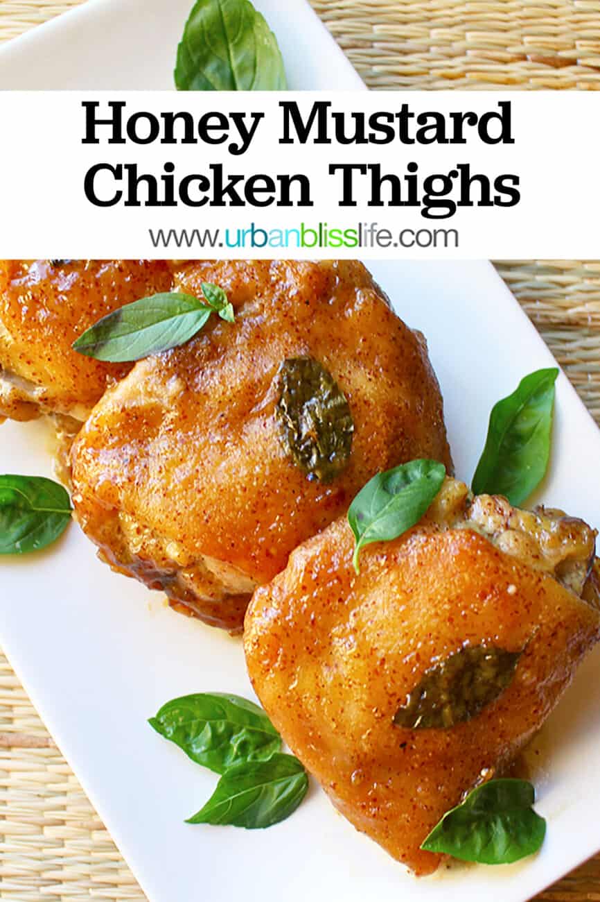 Three honey mustard chicken thighs with basil leaves on a white plate.