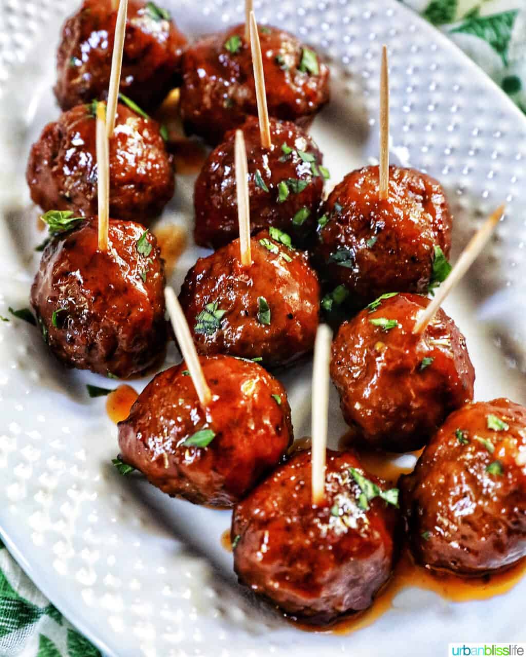 white serving plate with several honey bourbon meatball appetizers with toothpicks in them.