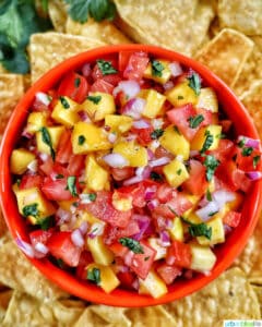 orange bowl filled with mango pico de gallo surrounded by pile of tortilla chips.