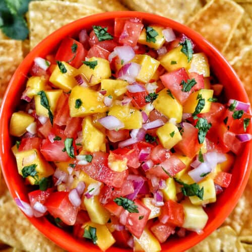 orange bowl filled with mango pico de gallo surrounded by pile of tortilla chips.