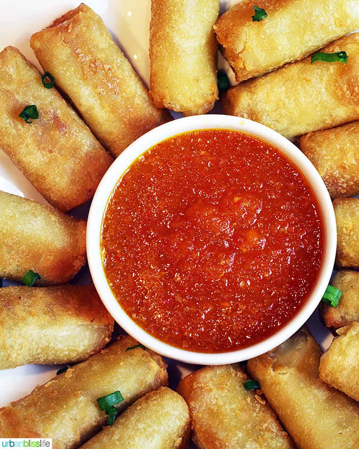 sweet chili dipping sauce in a bowl surrounded by egg rolls.
