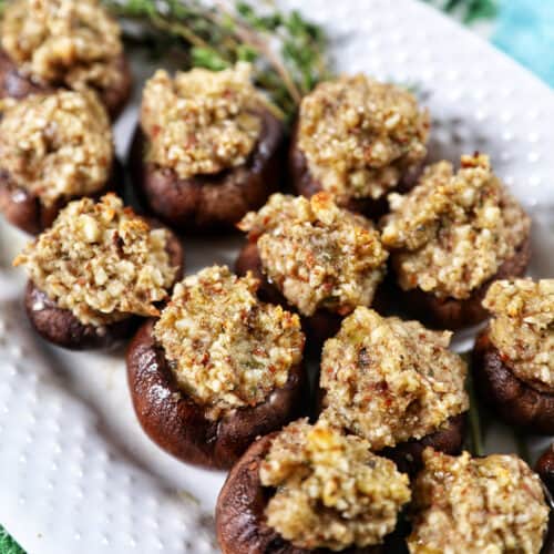 Vegan Stuffed Mushrooms close together on a white platter. with thyme leaves