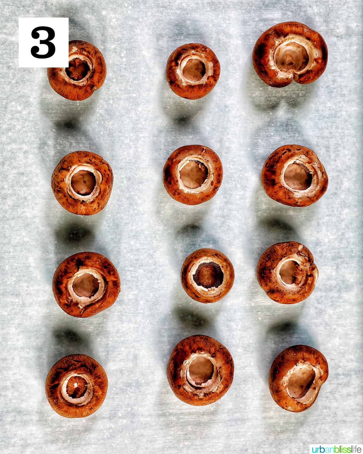 mushroom caps without their stems placed in four rows of three on a baking sheet.
