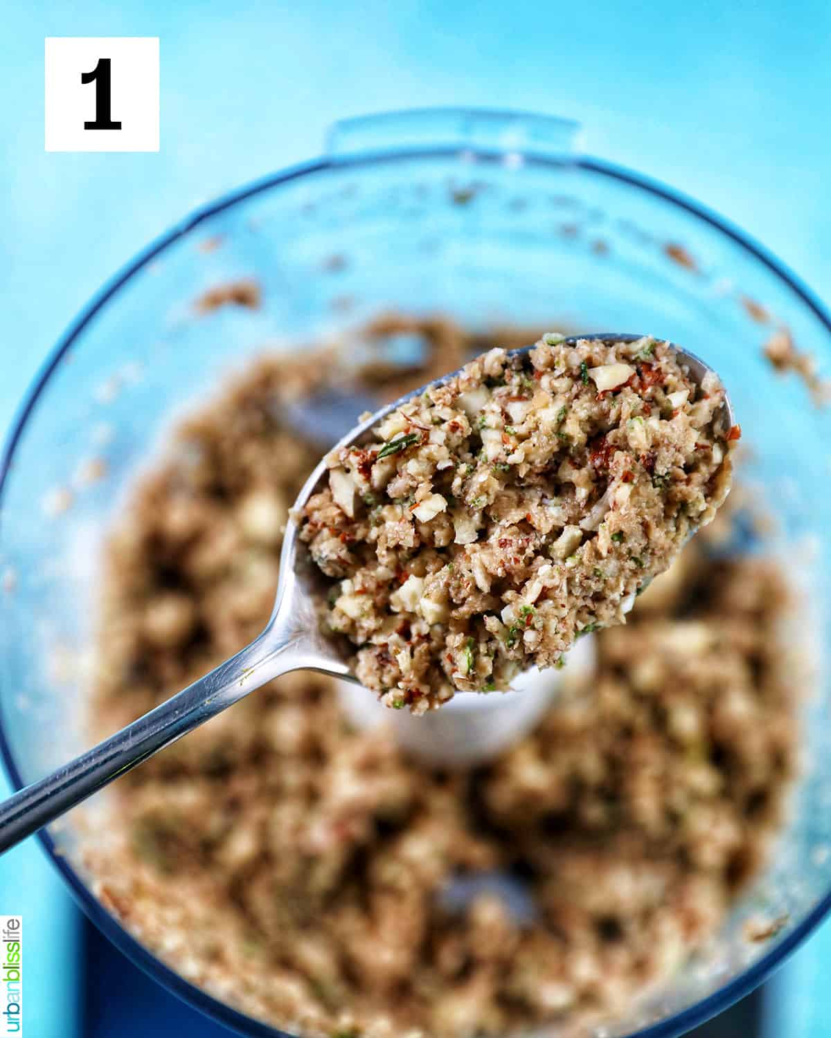 spoonful of filling for Vegan Stuffed Mushrooms above a food processor filled with stuffing blurred in the background.