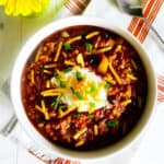 bowl of turkey chili with ground turkey, farro, stout, and toppings with a vase of yellow daisies.