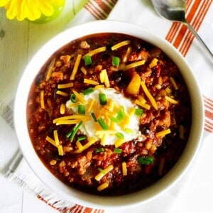 bowl of turkey chili with ground turkey, farro, stout, and toppings with a vase of yellow daisies.