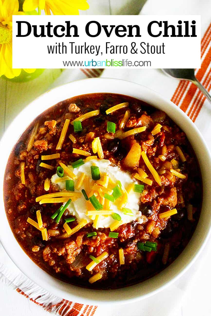 bowl of turkey chili with ground turkey, farro, stout, and toppings with a vase of yellow daisies with title text overlay.