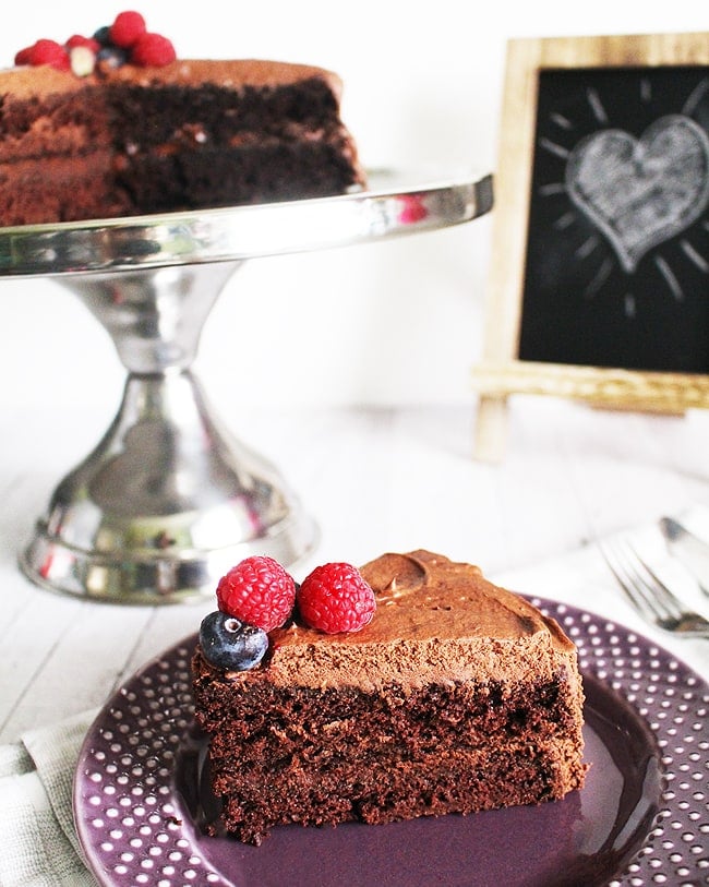 slice up close and full cake in background of vegan chocolate cake