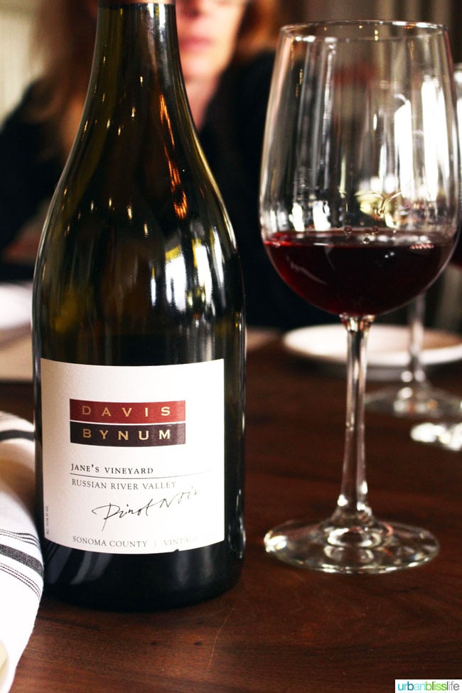 bottle of Davis Bynum wine with wine glass on a wood table.