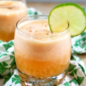 closeup side view of two glasses of cantaloupe margaritas with lime slice garnish on a green and white patterned napkin.