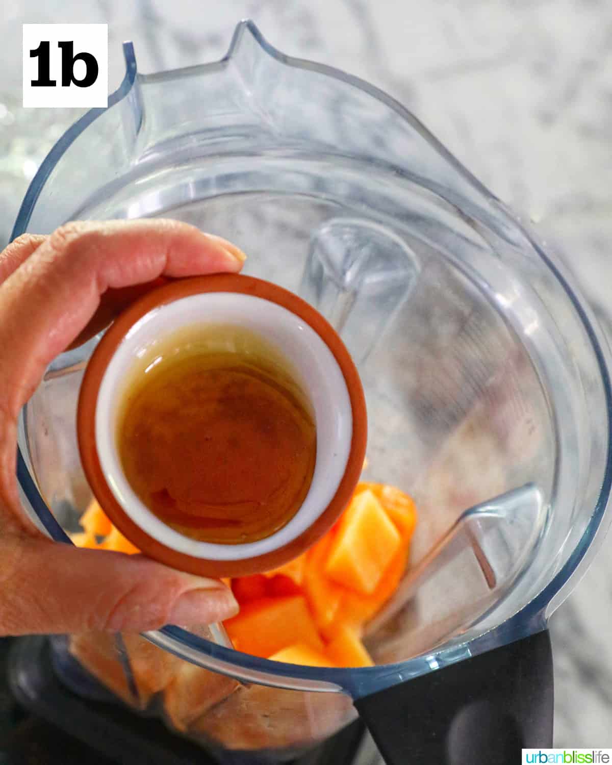 hand adding agave nectar to a blender with chopped cantaloupe.