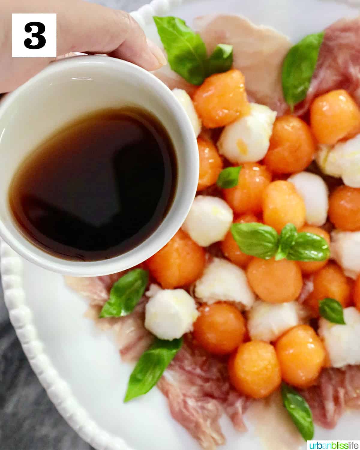 white bowl of balsamic vinegar to drizzle over melon prosciutto caprese salad in a white bowl.
