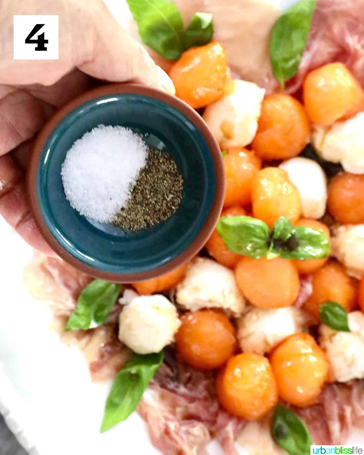 hand holding bowl of salt and pepper over melon prosciutto caprese salad.