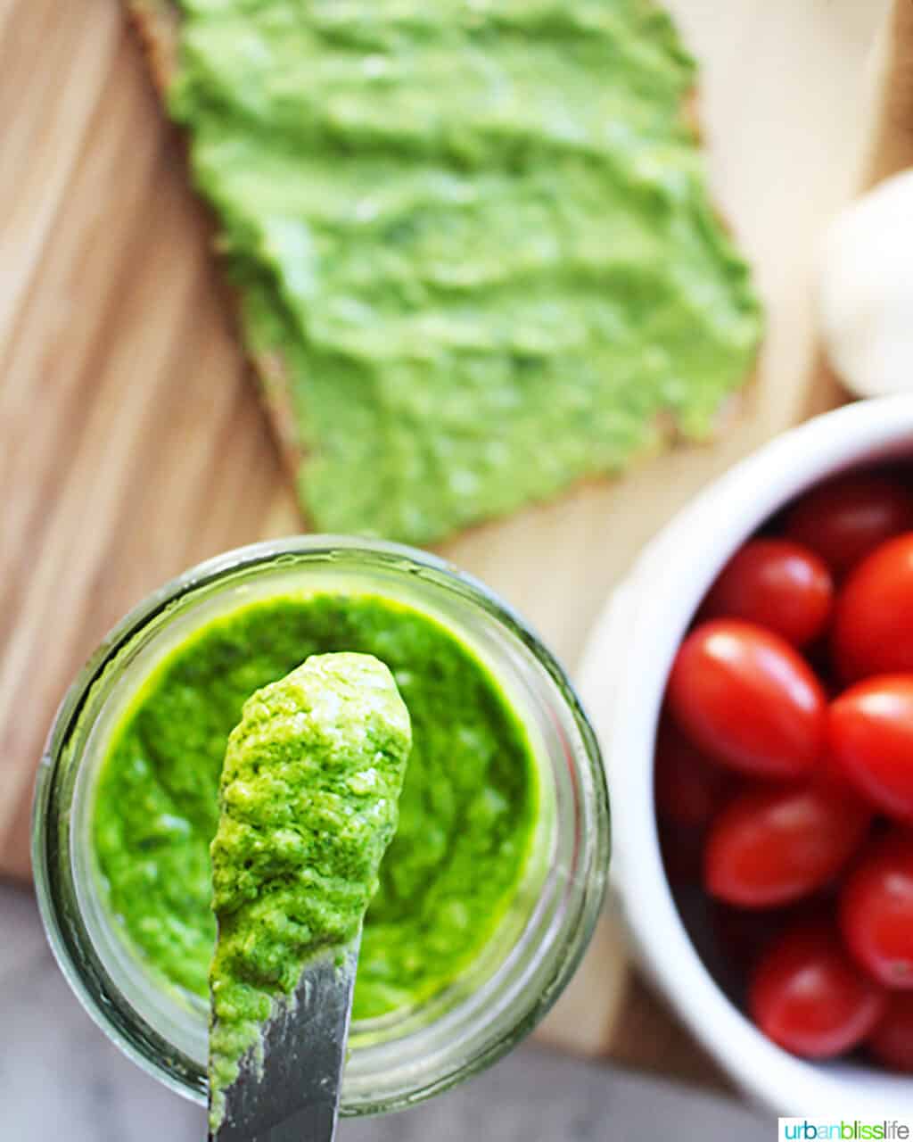 bright green avocado pesto in a mason jar with a small knife placed in the pesto.