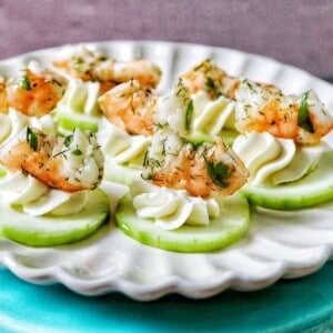 shrimp cucumber cream cheese appetizers on a scalloped plate.
