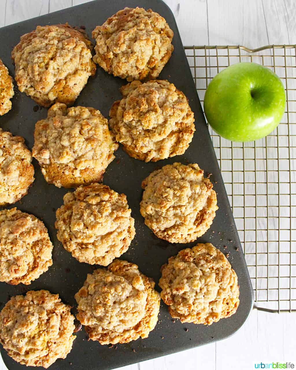 muffin tin with baked cinnamon streusel muffins and a green apple on the side.