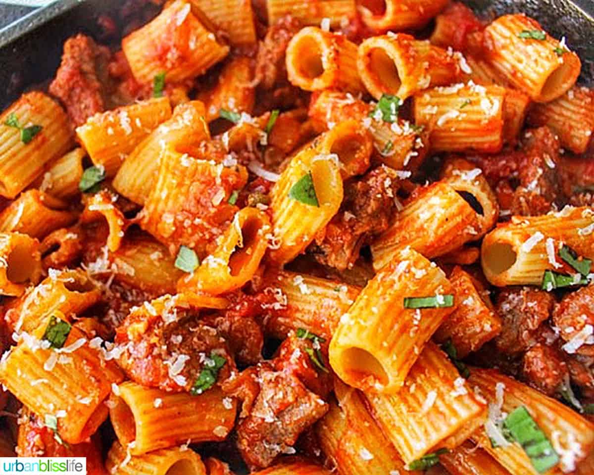 bowl of rigatoni pasta with Italian sausage in a cast iron skillet.