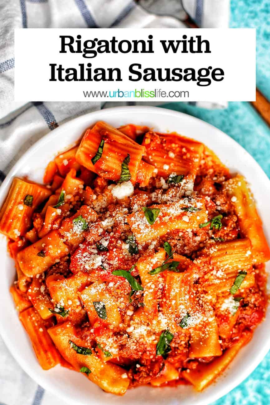 bowl of rigatoni pasta with Italian sausage on a white and blue checkered napkin and a fork with title text overlay.