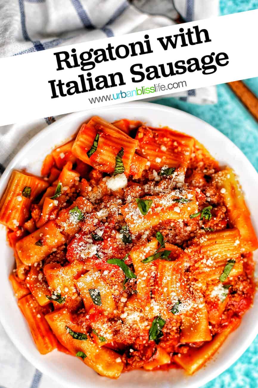 bowl of rigatoni pasta with Italian sausage on a white and blue checkered napkin and a fork with title text overlay.