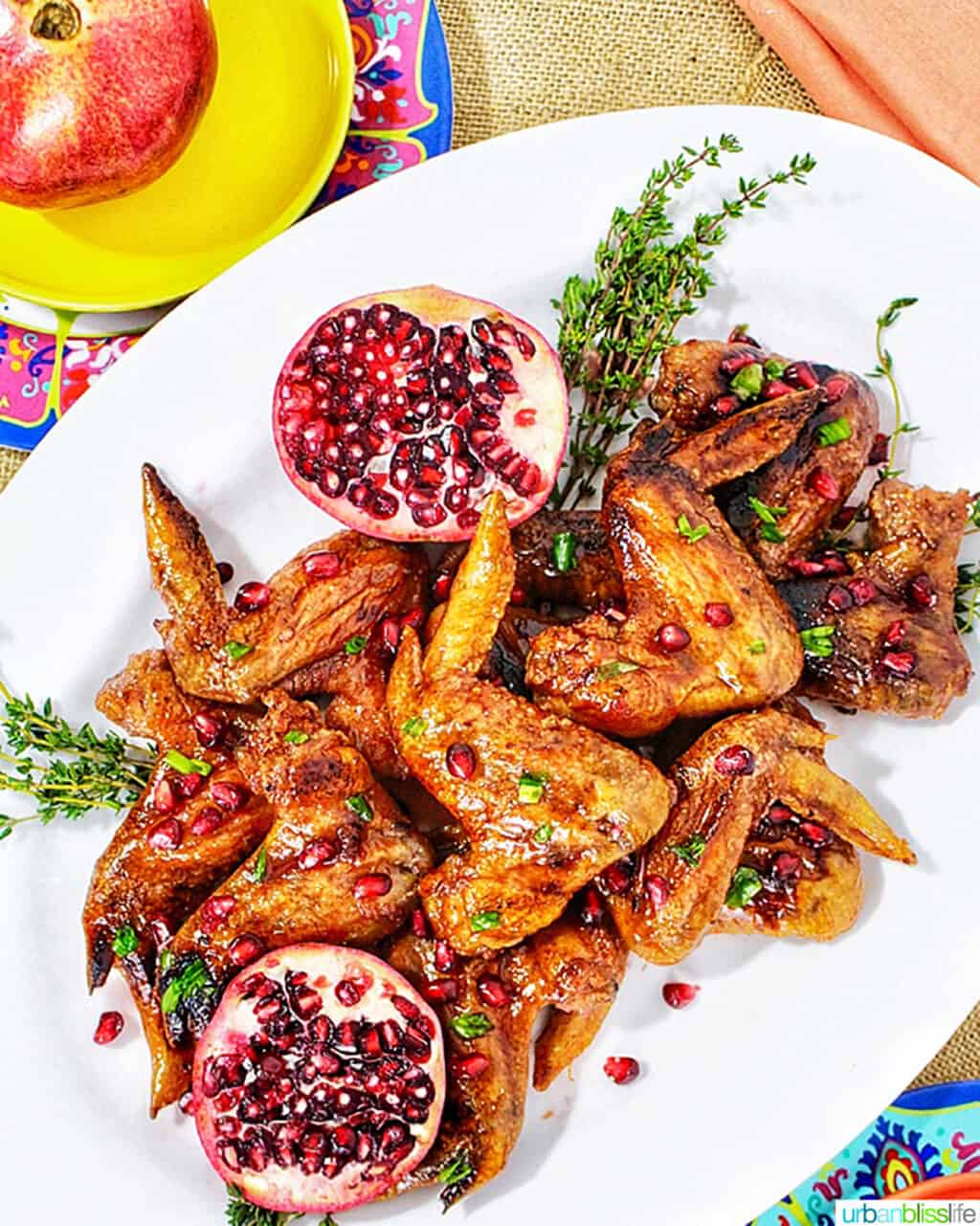 large platter of cranberry pomegranate sticky wings with a pomegranate halved on the side and herbs.