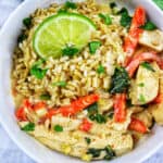 Thai coconut lime chicken with red bell pepper slices and lime slices over rice in a bowl.