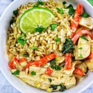 Thai coconut lime chicken with red bell pepper slices and lime slices over rice in a bowl.