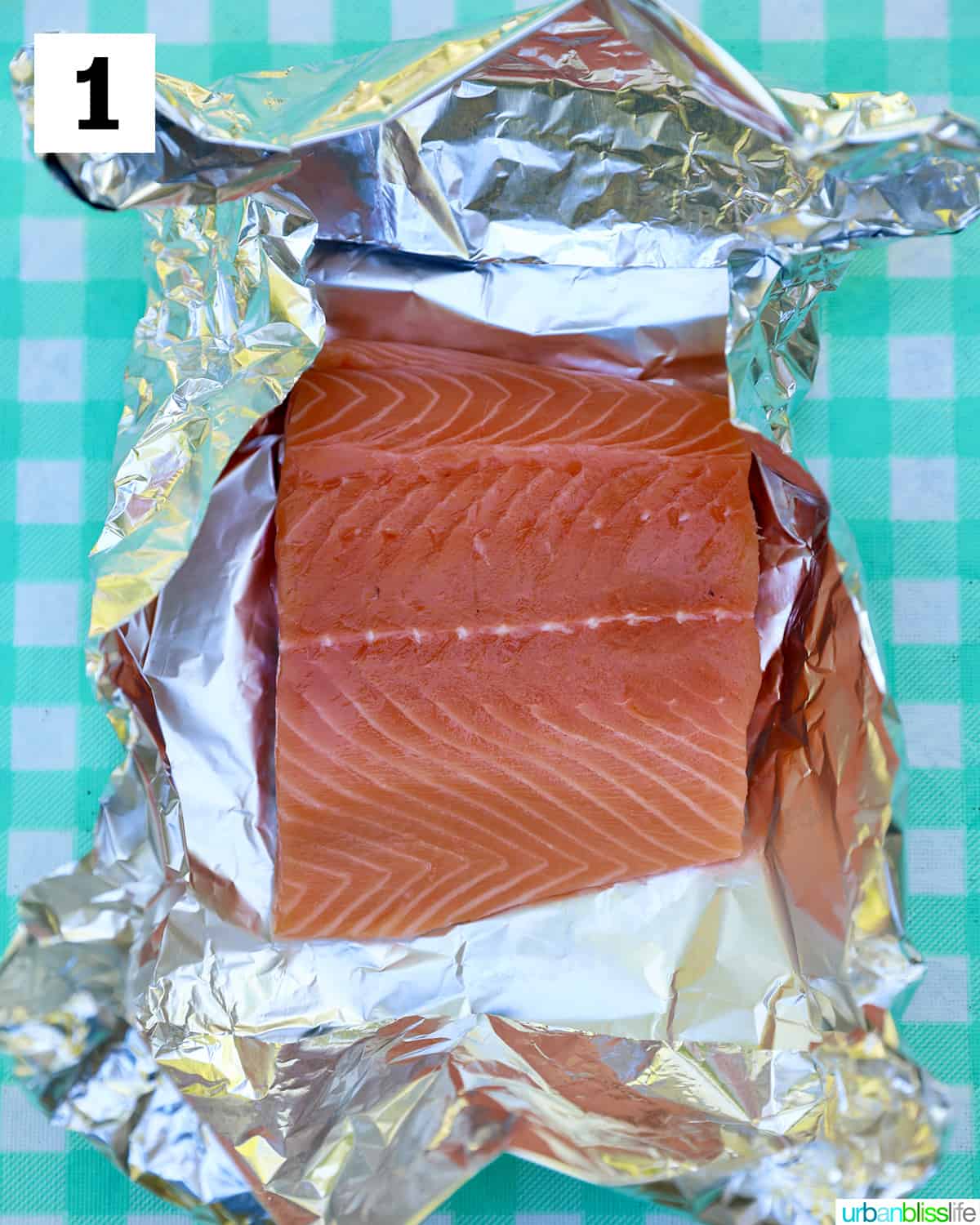 salmon filet placed in alumiinum foil on an aqua checkered tablecloth.