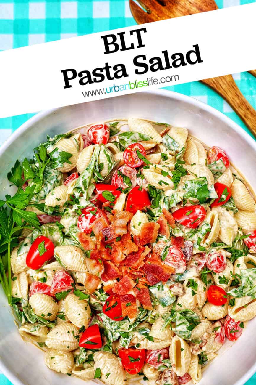 BLT pasta salad in a white bowl with wooden serving spoons overhead and title text overlay.