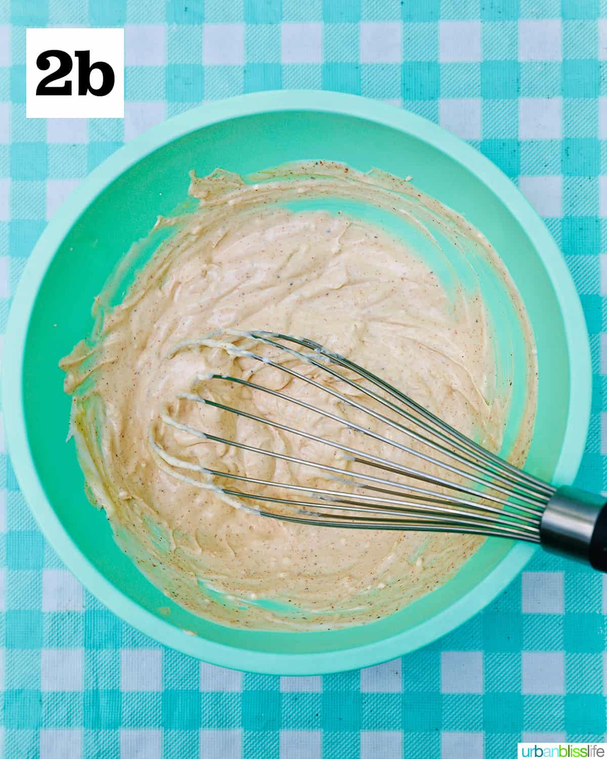 sauce for BLT pasta salad in a green bowl with whisk on an aqua checkered tablecloth.