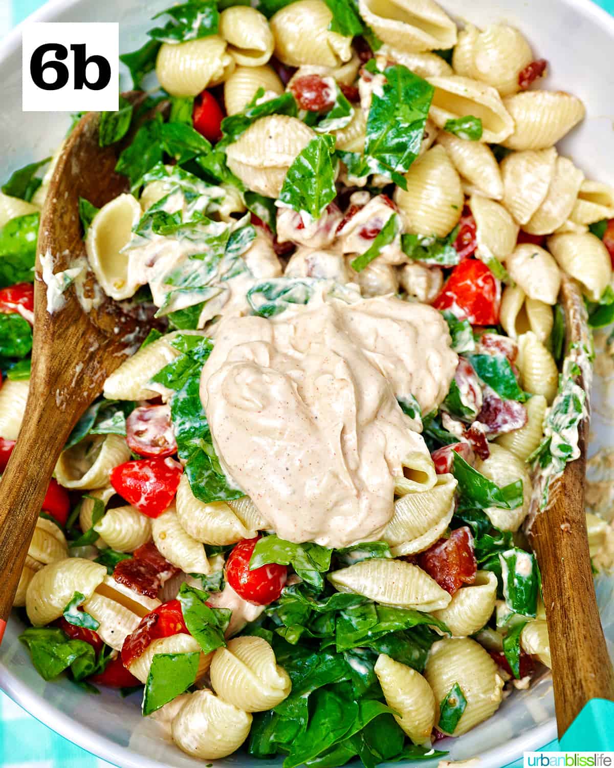 tossing together ingredients for BLT pasta salad with the salad dressing with wooden serving tongs.
