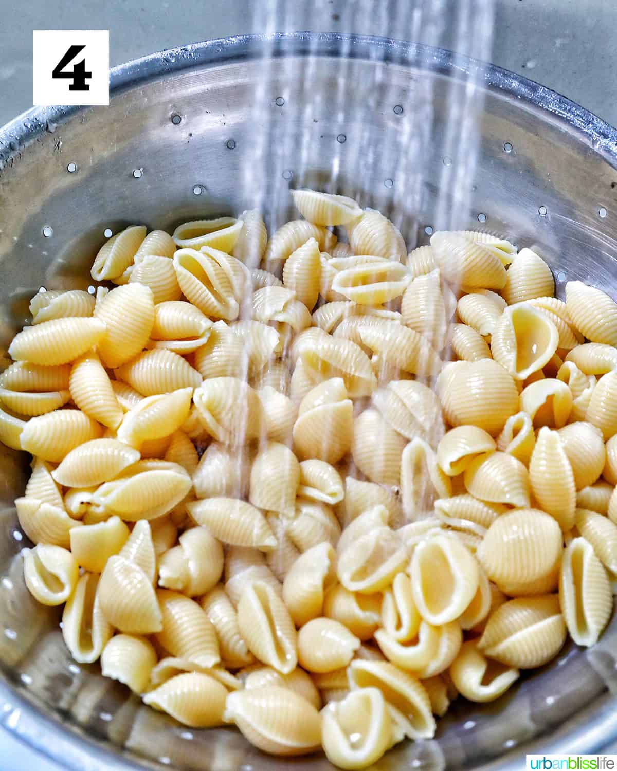 water streaming down on pasta shells in a strainer.
