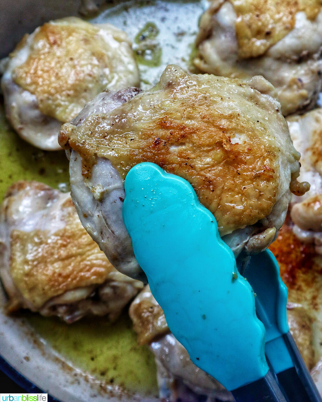 tongs holding chicken thighs.